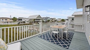 A deck with a table and chairs, surrounded by a white railing, overlooking a residential area with houses and a body of water. - Fish On - Channel Home Steps To The Beach (North Myrtle Beach)