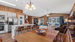 A modern kitchen with wooden cabinets, a central island, and a dining area with a wooden table and chairs. - Fish On - Channel Home Steps To The Beach (North Myrtle Beach)