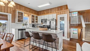 A modern kitchen with wooden paneling, stainless steel appliances, and a central island with bar stools. - Fish On - Channel Home Steps To The Beach (North Myrtle Beach)