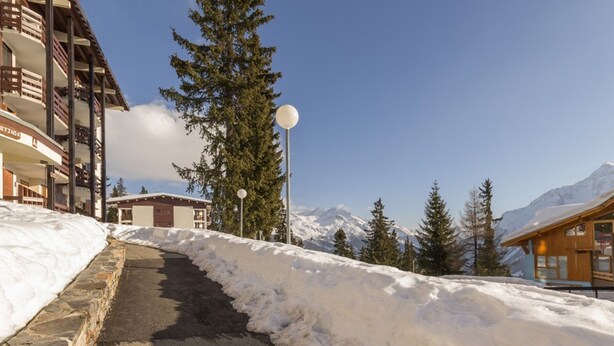 Un sentier enneigé menant à un bâtiment d’où l’on a une vue sur la montagne.