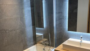 Un baño moderno con ducha envuelta en vidrio, una bañera blanca y un tocador de madera con lavamanos.