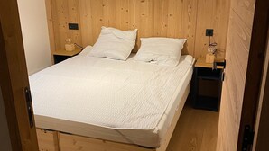 Una cama de madera con colchón y almohadas blancas, dos mesitas de noche y un cabecero de madera.