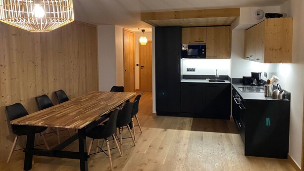 Una cocina moderna con una isla central, mesa de comedor de madera con sillas y una lámpara colgante.