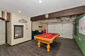 Una mesa de billar en una habitación con techo de madera, un sofá y una puerta.