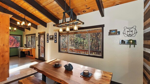 A wooden dining area with a large table, benches, and a view of trees through a window. - Big Bear Escape By Destination Big Bear: Modern Cabin Elegance! Gameroom! Hot Tub! Fenced Yard! (Big Bear Lake)