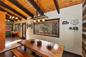 A wooden interior with a large dining table, benches, and a view through a window.