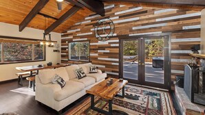 A cozy living room with a wooden ceiling, a sofa, a coffee table, and a large window. - Big Bear Escape By Destination Big Bear: Modern Cabin Elegance! Gameroom! Hot Tub! Fenced Yard! (Big Bear Lake)