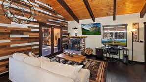 A cozy living room with a fireplace, a large clock, and a TV. - Big Bear Escape By Destination Big Bear: Modern Cabin Elegance! Gameroom! Hot Tub! Fenced Yard! (Big Bear Lake)