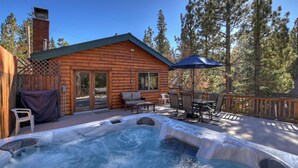 A log cabin with a hot tub, outdoor seating, and a deck surrounded by trees. - Big Bear Escape By Destination Big Bear: Modern Cabin Elegance! Gameroom! Hot Tub! Fenced Yard! (Big Bear Lake)