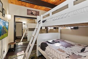 Habitación con literas, una escalera de acceso, un cuadro en la pared y techo de madera.