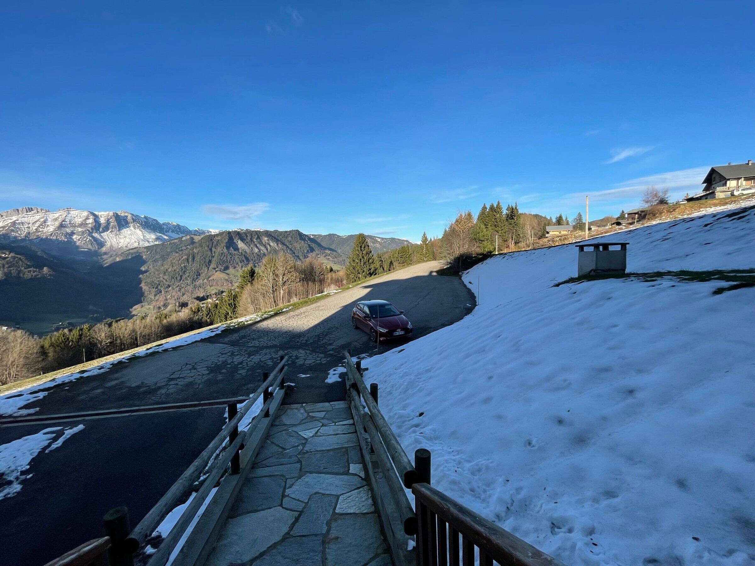 A snow-covered road with a car parked on the side, leading to a mountain view.