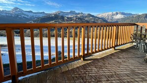 Eine Holzdielen-Terrasse mit Geländer, die auf eine schneebedeckte Landschaft und Berge blickt.