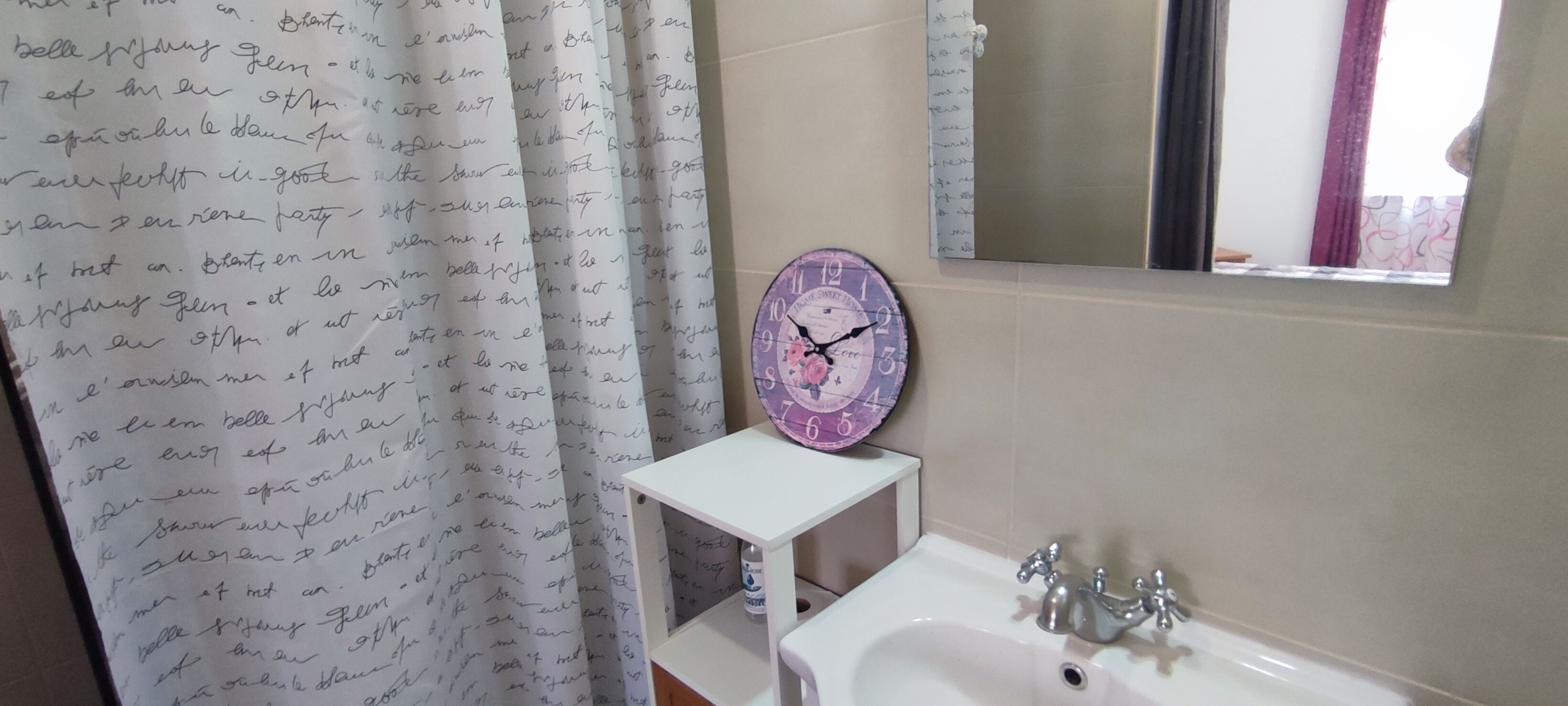 A bathroom with a white sink, a mirror, a clock, and a shower curtain with handwritten text.