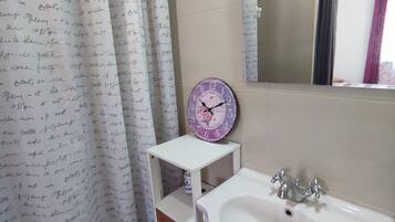 A bathroom with a white sink, a mirror, a clock, and a shower curtain with handwritten text.