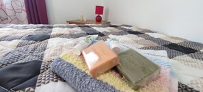 En seng med et mønstret quilt, et lille natbord med en rød lampe og to sæber.