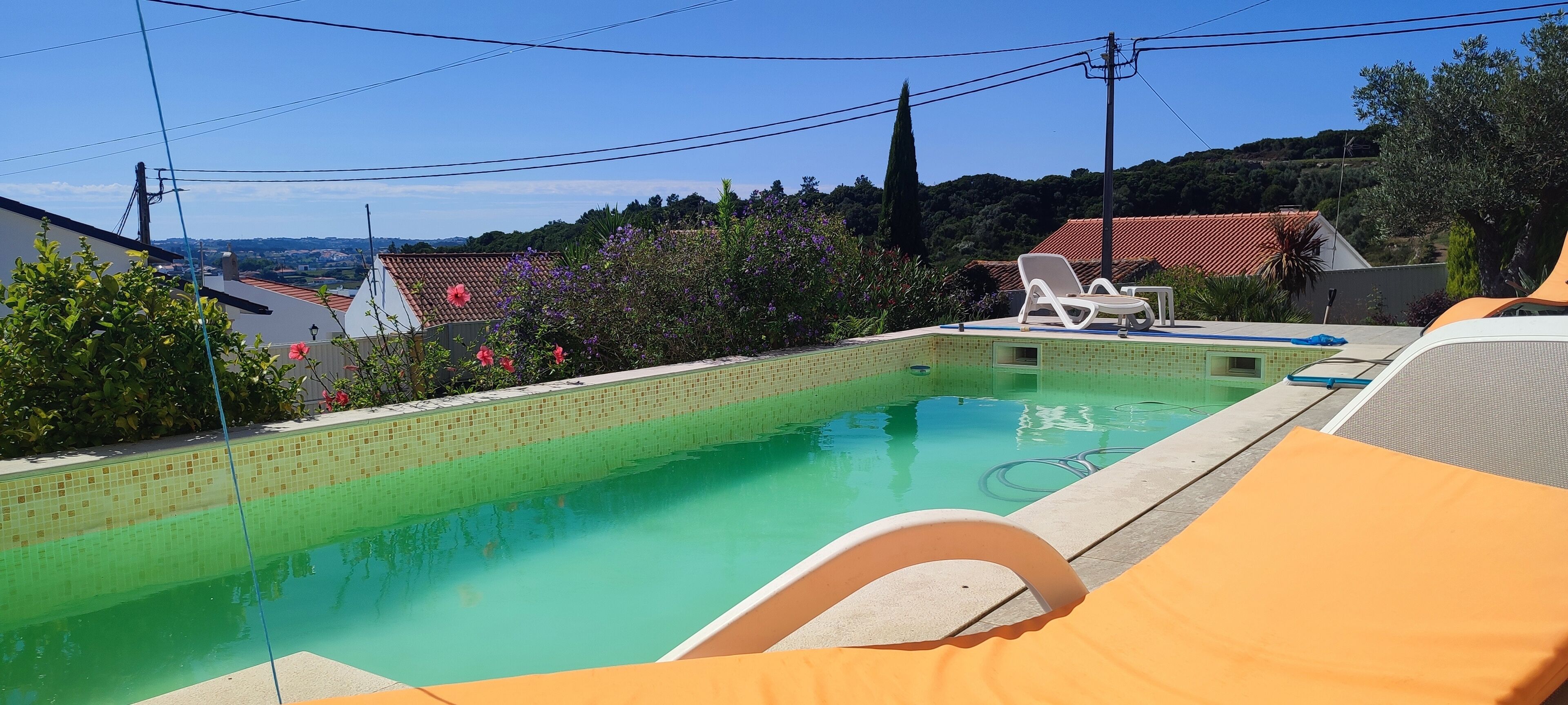 Une piscine dont les bords sont recouverts de carreaux, entourée de mobilier d’extérieur et de verdure.