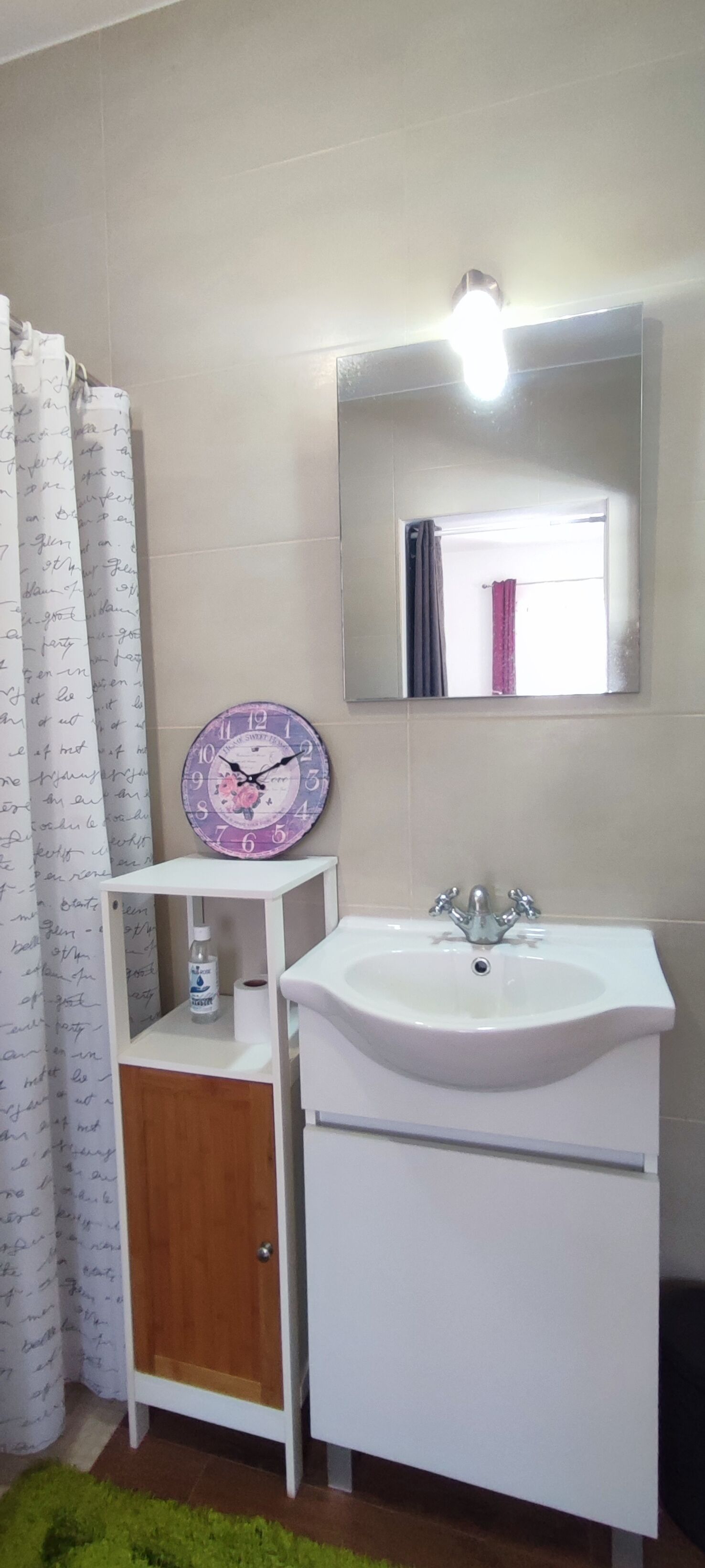 Un baño con lavamanos blanco, espejo, reloj y cortina de ducha.