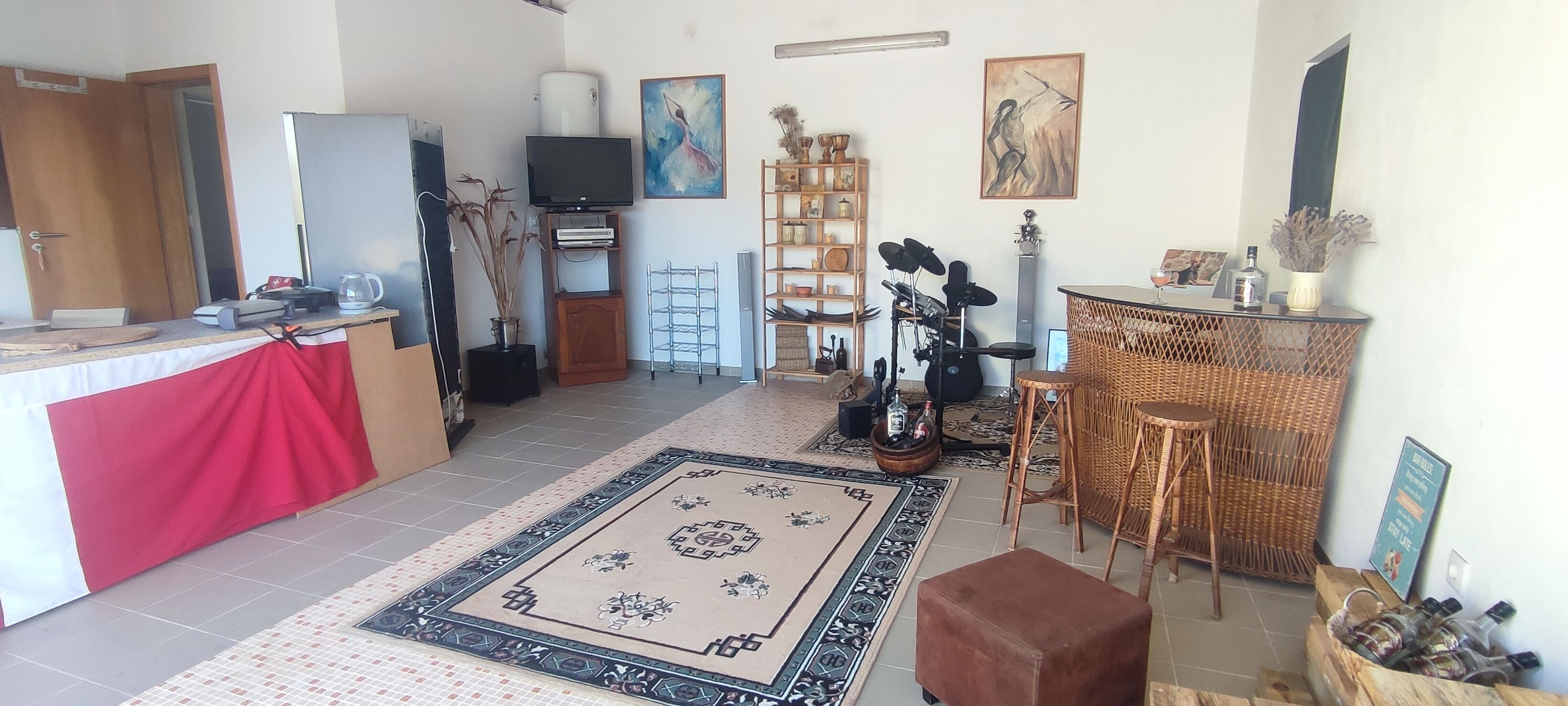 A compact living space with a kitchenette, a dining area with wicker furniture, and a TV mounted on the wall.