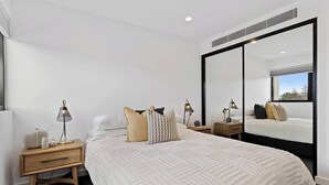 A modern bedroom with a large bed, bedside tables, lamps, and a large mirror. - Sleek City Pad with a Garden Rooftop (Hobart)