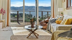 Un salón con puerta de cristal que da a un balcón con vistas a un lago y montañas.
