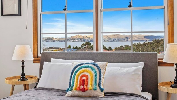 Un dormitorio con una cama, dos lámparas de noche, un ventanal con vistas a colinas y un lago.