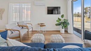 A modern living room with a sofa, two armchairs, a small side table, a potted plant, and a large window with a view.