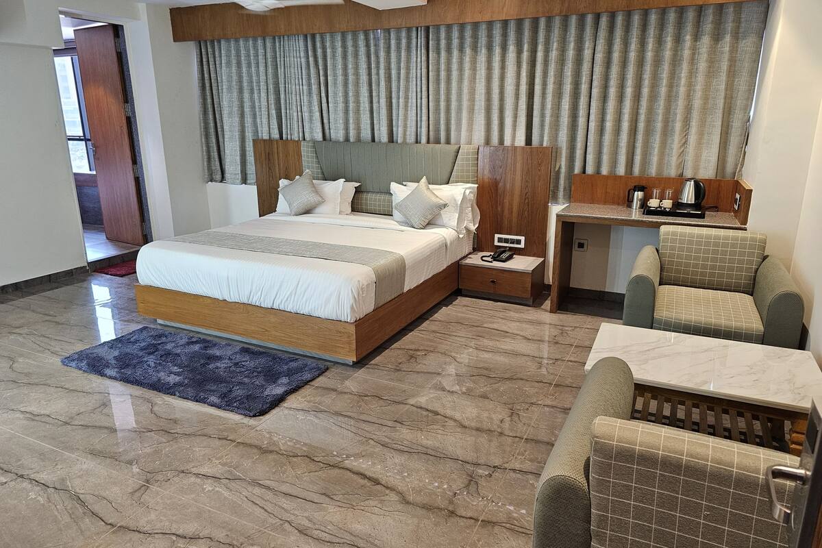 A modern hotel room with a large bed, a desk, and two armchairs.