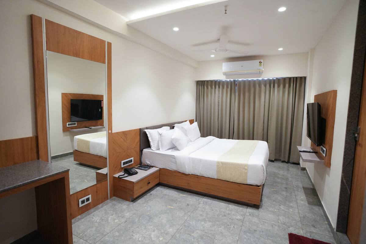 A modern hotel room with a large bed, a desk, a mirror, a television, and an air conditioning unit.