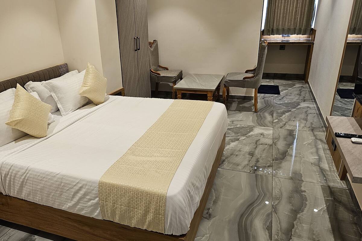 A hotel room with a large bed, a wooden nightstand, a desk, and a chair.