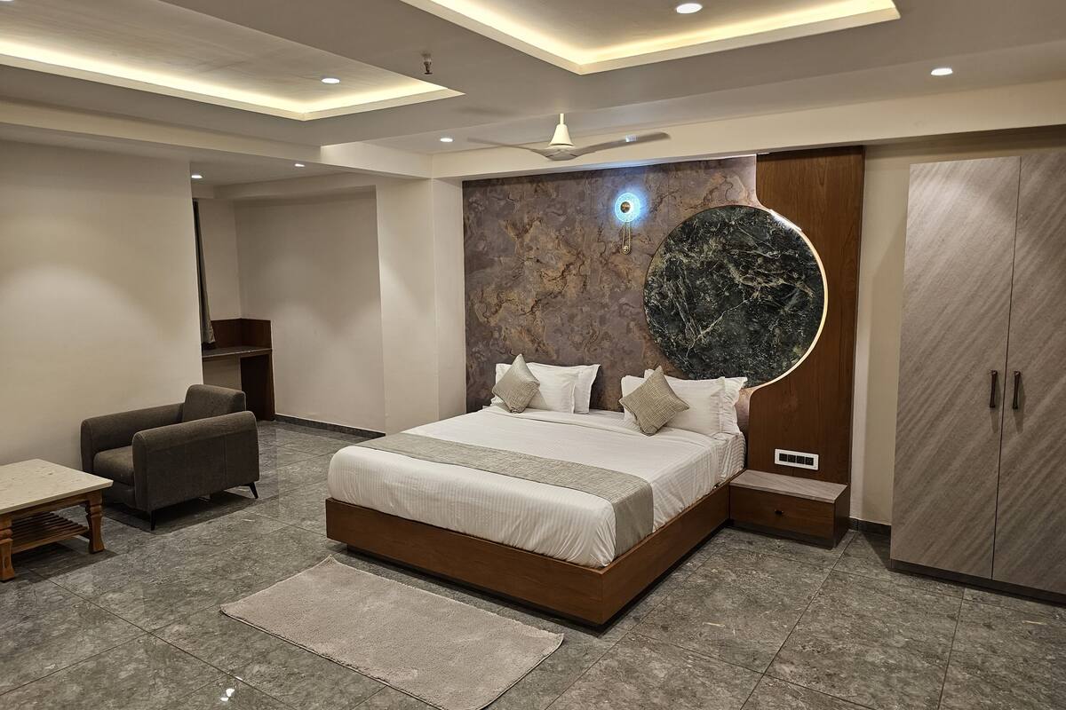 A modern bedroom with a large bed, a round mirror, a wardrobe, and a seating area.