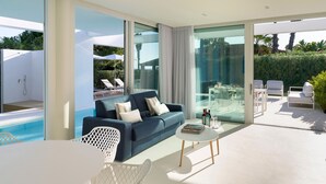 A modern living room with a blue sofa, white coffee table, and glass doors leading to a pool area. - Beautiful modern villa with private pool, just steps from the sea in Fanusa, Syracuse. (Siracusa)