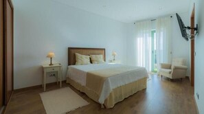 Een slaapkamer met een bed, nachtkastjes, een stoel en een aan de muur bevestigde televisie.