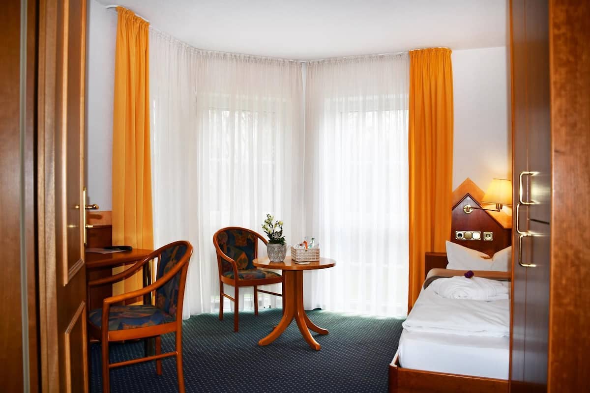 Ein Hotelzimmer mit einem Bett, einem Schreibtisch mit Stuhl, einem kleinen Tisch mit Pflanze und einer Lampe.