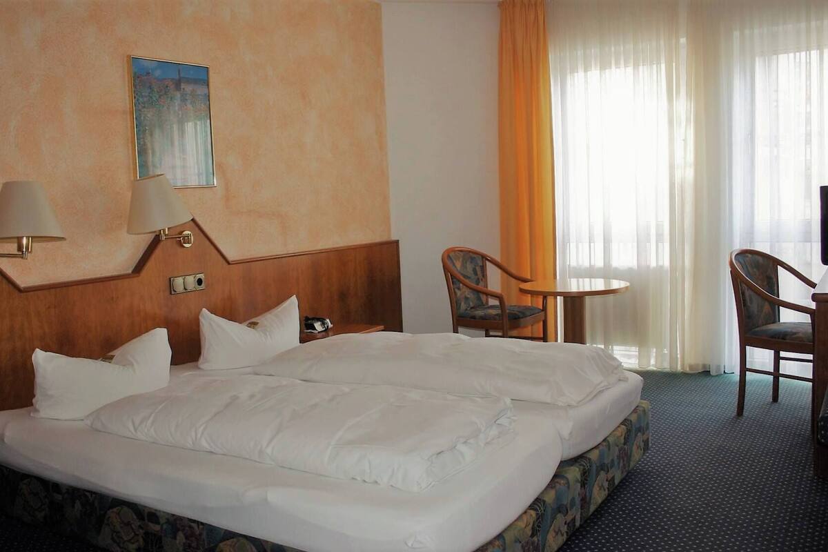 Ein Hotelzimmer mit einem großen Bett, zwei Stühlen, einem kleinen Tisch und einem Fernseher.