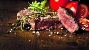 Un steak au romarin et aux grains de poivre, présenté sur une surface en bois.