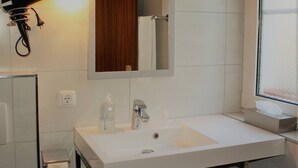 Une salle de bain moderne avec un lavabo blanc, un miroir, un sèche-cheveux et un porte-serviettes.