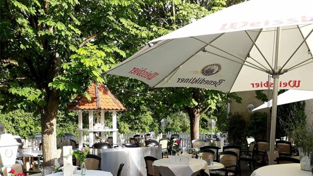 Un espace de restauration en plein air avec des tables protégées par des parasols, entouré d’arbres et agrémenté d’un belvédère.