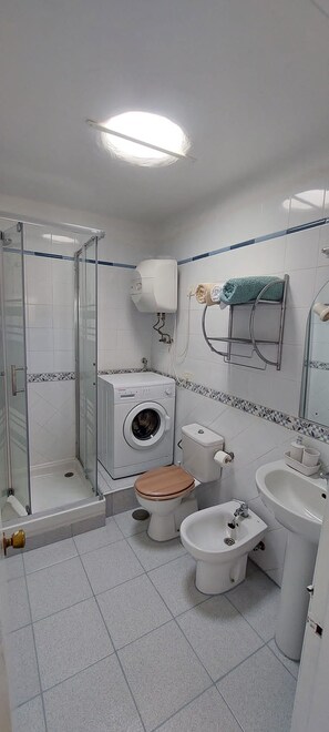 A bathroom with a glass-enclosed shower, a washing machine, a toilet, a bidet, and a sink. - Ocean View Sunset Terrace Anfi del Mar (Los Caideros)