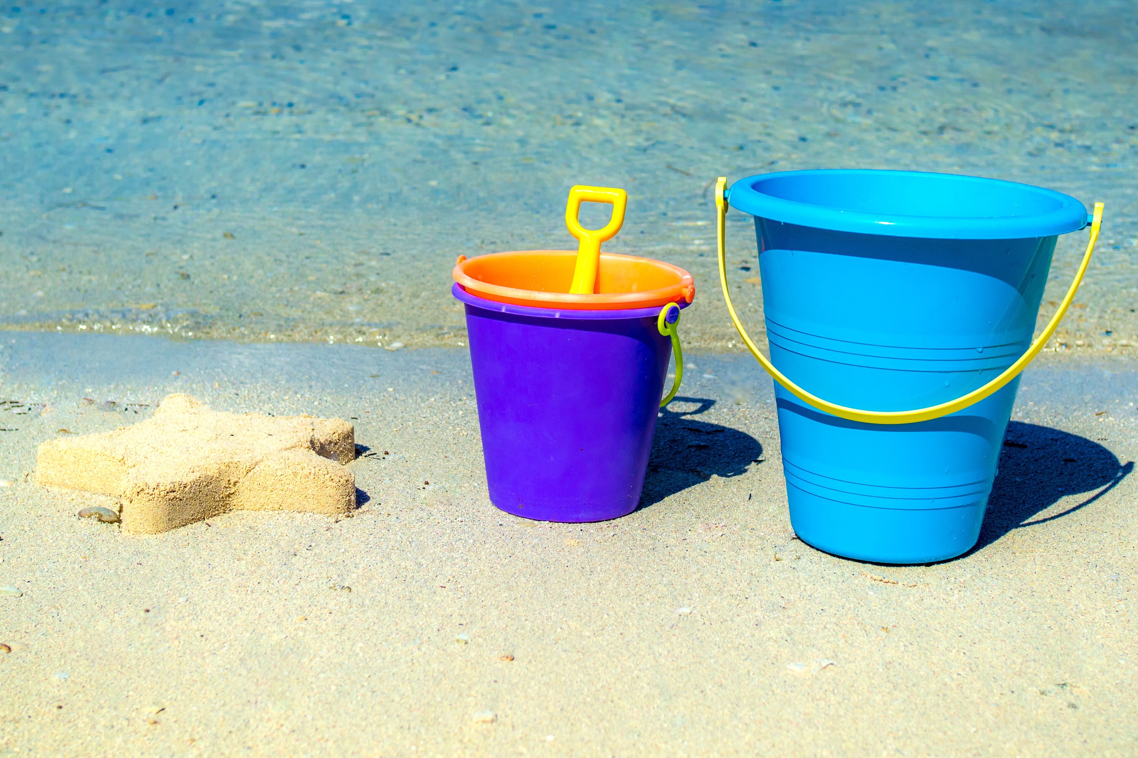 Um balde roxo com cabo amarelo e um balde azul com cabo amarelo numa praia arenosa.