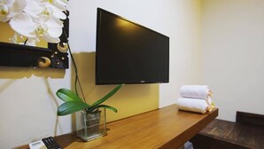 Una habitación de hotel con una consola de madera, un televisor en la pared, una planta en maceta, un control remoto y un juego de toallas.