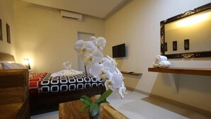 Habitación de hotel con cama, mesita de noche de madera, espejo y televisión montada en la pared.