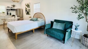 Une chambre à coucher moderne avec un lit en bois, un canapé vert, une suspension ronde et une plante en pot.
