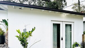 Une maison blanche avec une porte-fenêtre coulissante, une terrasse en bois et diverses plantes.