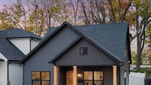 A two-story house with a dark gray exterior, a front porch with a wooden door, and a stone retaining wall.