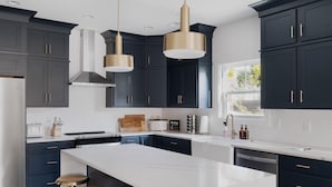 A modern kitchen with dark cabinets, white countertops, gold fixtures, and a central island with stools.
