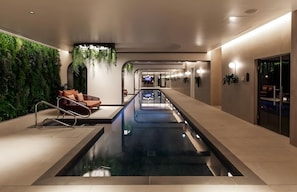 A modern indoor pool area with a long, narrow pool, a seating area with a sofa and cushions, and a wall with vertical greenery.