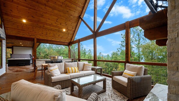 A spacious covered patio with wicker furniture, a glass coffee table, and a stone fireplace.