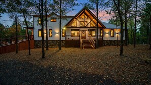 A two-story cabin with a prominent front porch, wooden deck, and a stone foundation.