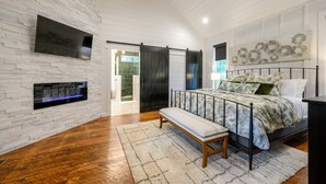 A bedroom with a bed, bench, TV, and artwork on the wall.