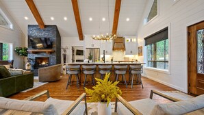 A spacious living area with a fireplace, a large TV mounted on a stone wall, and a bar area with stools.